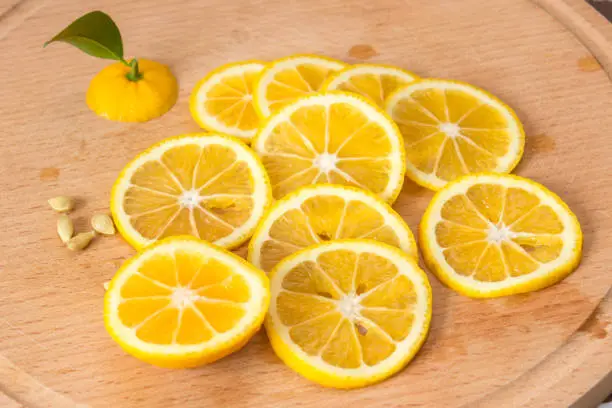 Sliced orange-yellow lemon of Volkamer with a small green leaf and seeds on a wooden board, indoor culture of growing citrus plants, close-up