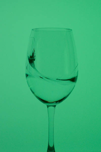 istock Wine glass on a long stem. A little drink is poured into it, a splash is visible. In back green. 1163026844