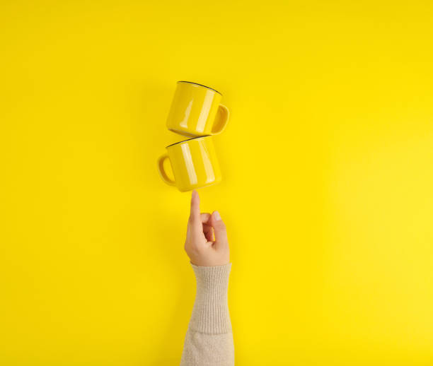 istock two yellow ceramic cups are supported by a female hand on a yellow background 1163029454