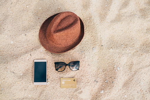 Sunglasses, hat, smart phone and credit card on the sand on the beach. Beach accessories - Vacation Concept.