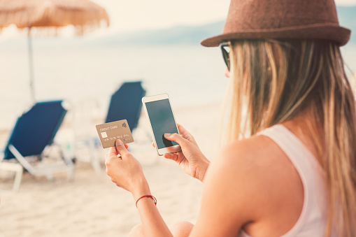 Woman holding credit card and smart phone on the beach