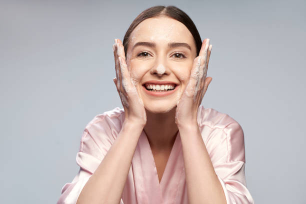 cheerful pretty girl washing face with foaming cleanser - facial cleanser imagens e fotografias de stock
