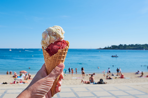 hand is holding ice cream cone in front of a beach in Brittany, France