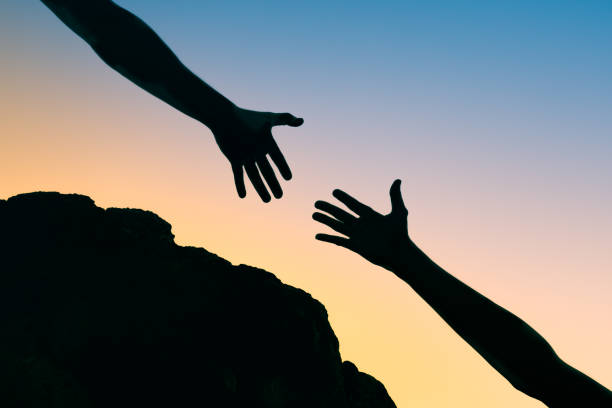 Helping hands Persons hand reaching out to help another hand up a mountain cliff. humanitarian aid stock pictures, royalty-free photos & images