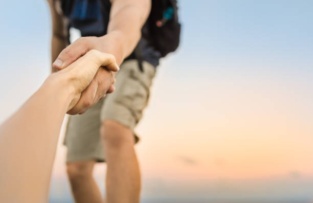 Giving a helping hand Hiker giving his hand helping partner climb up to the top of mountain. a helping hand stock pictures, royalty-free photos & images