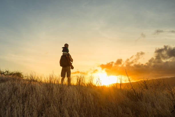 Father and son hiking through the mountain at sunrise Father son on an adventure hiking through the mountain side at sunrise. on shoulders stock pictures, royalty-free photos & images