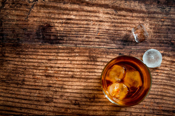 Alcoholic beverage and drinking establishment concept theme with a top view or above the tabletop image of a glass of bourbon whiskey on a wood table in a rustic bar with copyspace Alcoholic beverage and drinking establishment concept theme with a top view or above the tabletop image of a glass of bourbon whiskey on a wood table in a rustic bar with copy space pub table top view stock pictures, royalty-free photos & images