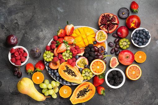 Delicious fruit platter mango pomegranate raspberries papaya oranges passion fruits berries on oval serving plate on dark concrete background, selective focus, top view, copy space