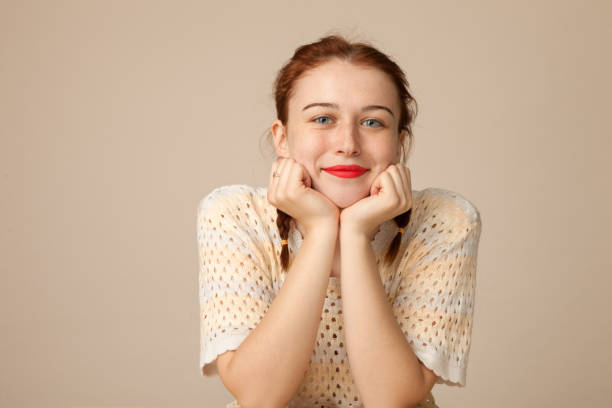 Studio portrait of a 20 year old attractive red-haired woman on a beige background Studio portrait of a 20 year old attractive red-haired woman on a beige background teenage girls pretty smile looking at camera waist up stock pictures, royalty-free photos & images