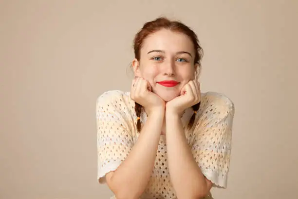Studio portrait of a 20 year old attractive red-haired woman on a beige background