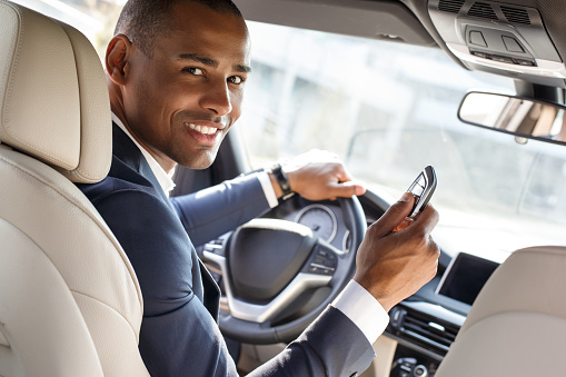 Young african american businessman driver sitting inside the car holding alarm controller looking camera smiling happy view from the back seat