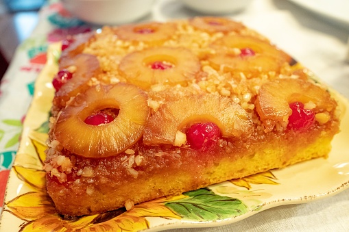 Close-up of pineapple upside down cake with pineapples, cherries, coconut and crust on floral patterned dish, July 16, 2019