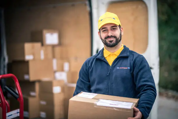 Smiling delivery man in uniform holding cardboard box looking at camera.