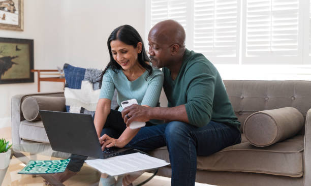 le couple mature assis ensemble sur un canapé et à l'aide d'un ordinateur portable pc pour les achats en ligne ou appel vidéo via internet. - senior adult comfortable relaxation latin american and hispanic ethnicity photos et images de collection