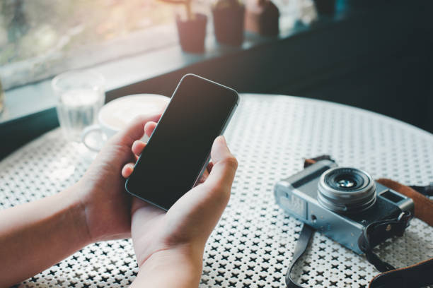 main de femme utilisant le smartphone dans le café et l'appareil-photo sur la table - retro revival telephone human hand toned image photos et images de collection