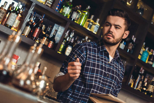 istock Young bartender standing at bar counter holding pen and notebook thoughtful 1163065619