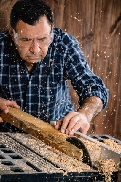 istock Male Hispanic carpenter using saw in home workshop with wood chips flying and protective eyewear 1163069443
