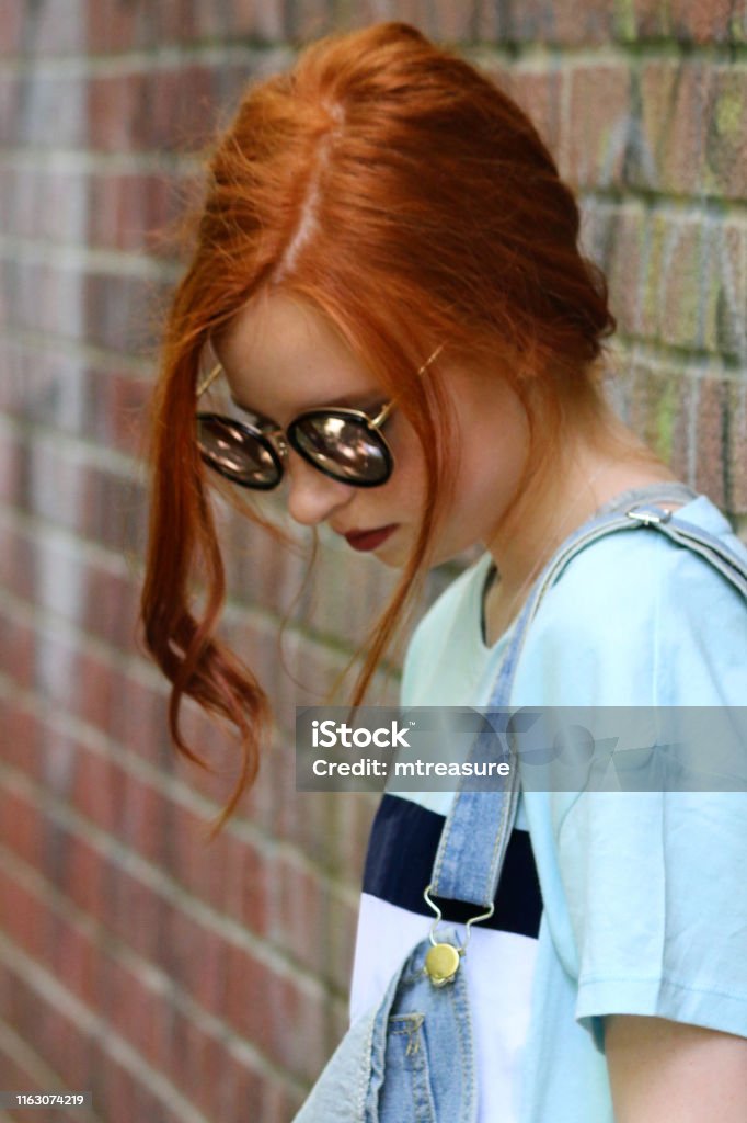 Image Of Pretty Moody Sad Teenage Girl Youth With Red Hair Looking Down  Lost In Thought By Brick Wall With Graffiti Redhead Wearing Blue Denim  Dungarees Sunglasses Makeup Dark Red Lipstick Teenager