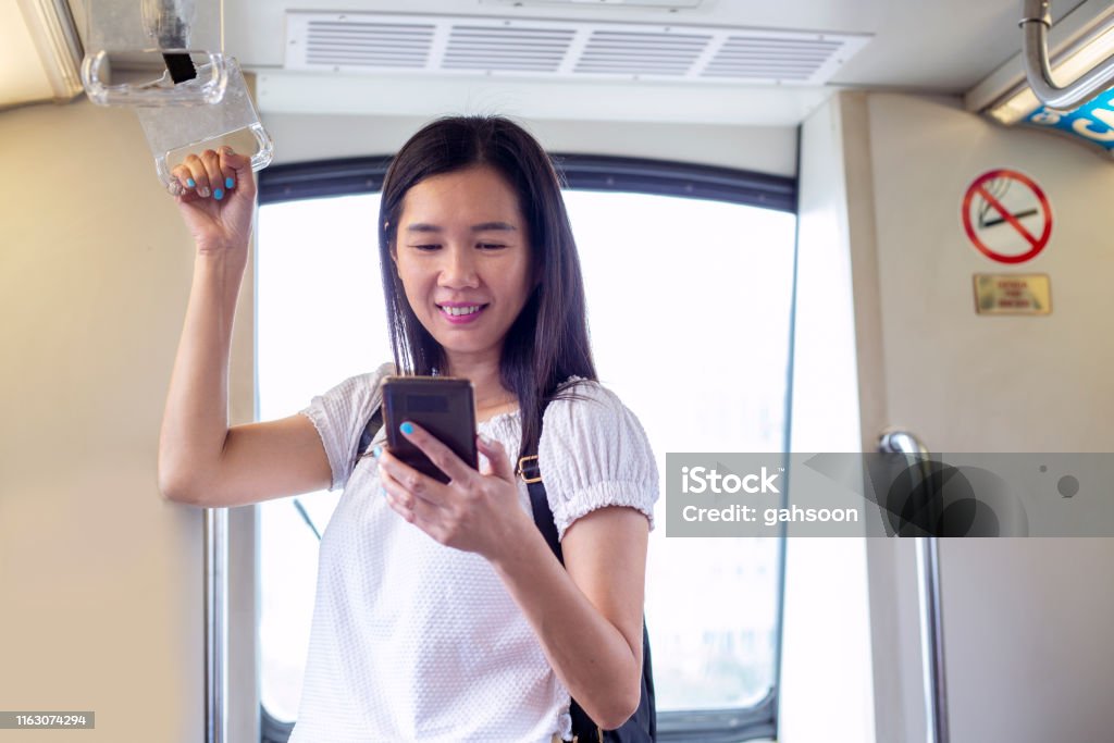 Woman uses mobile app while riding MRT commuter train Asian, Woman, MRT, Airport, Smiling, Asian and Indian Ethnicities Stock Photo
