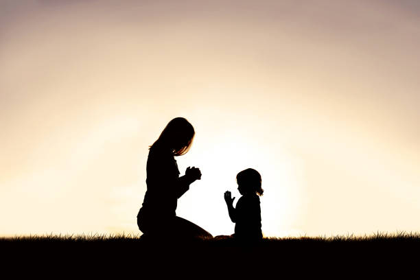 Mother Praying with her Young Child Outside at Sunset. stock photo