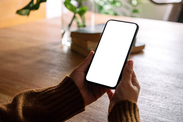istock Mockup image of hands holding black mobile phone with blank desktop screen on wooden table 1163084958