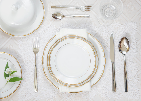 Beautifully decorated table with white plates, crystal glasses, linen napkin and cutlery are on luxurious tablecloths; top view