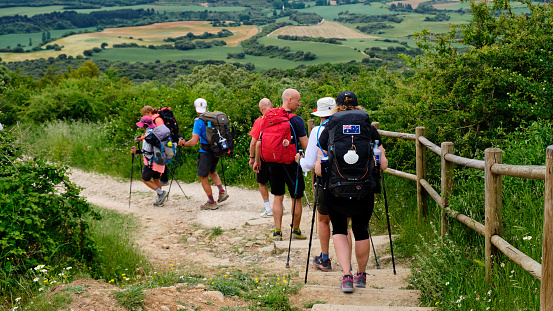Navarre, Spain, June 3, 2019: Pilgrims walking on the Camino de Santiago. Group of internaltional pilgrims starting the descent from Alto del Pardon towards plains of Navarra
