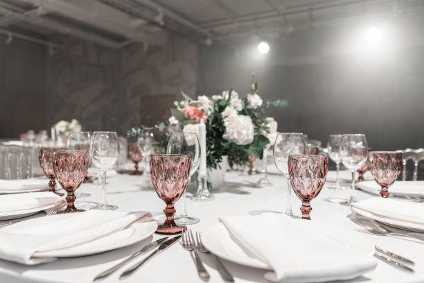 istock Wine glasses on round Banquet table served. Interior of restaurant for wedding dinner, ready for guests. Decorated with floral arrangement. Dishes, wine glasses and napkins. Catering concept. 1163093400
