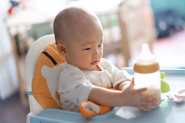 bebê asiático bonito com frasco de leite e na cadeira elevada - chilhood - fotografias e filmes do acervo