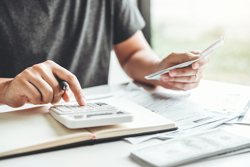 Hombre usando calculadora Cálculo de contabilidad Costos Facturas económicas con pila de dinero paso creciente crecimiento ahorrando dinero en casa, concepto financiero photo