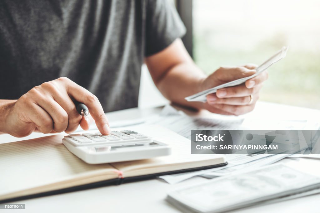 Man using calculator Accounting Calculating Cost Economic bills with money stack step growing growth saving money in home , finance concept Finance Stock Photo