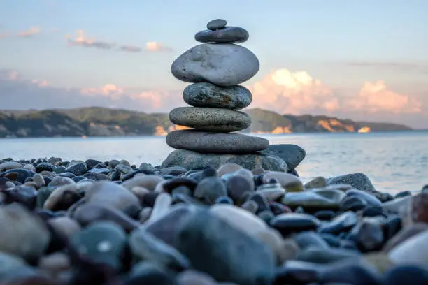 pyramid of stones on a pebbly beach, in the background the mountains and the sea