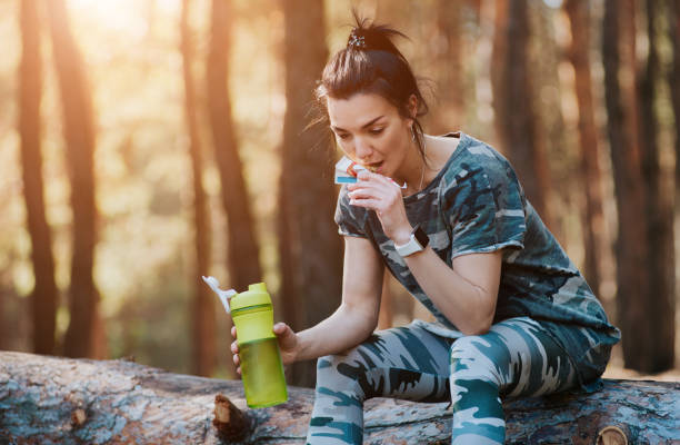istock woman drinks amino acids and has a protein bar in the forest 1163124117