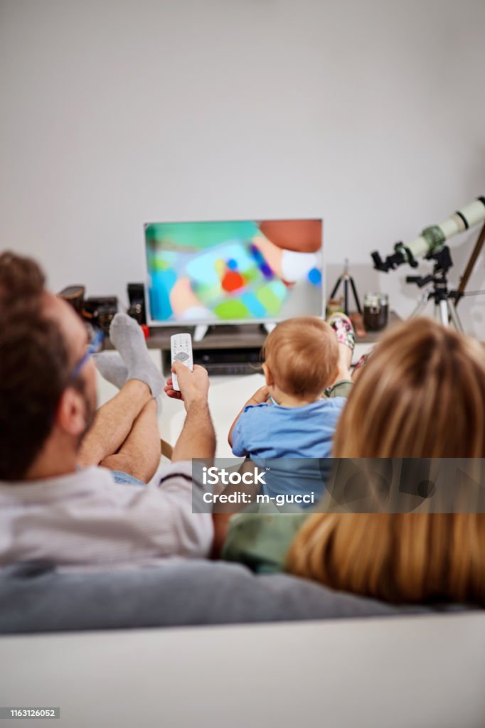 Young parents watching TV with baby boy. Television Set Stock Photo