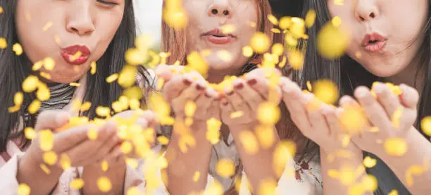 Happy asian friends having fun throwing confetti at party outdoor - Young trendy people enjoying fest event - Hangout, friendship, trends and youth concept - Focus on center girl face