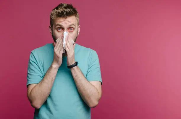 Photo of studio picture from a young man with handkerchief. Sick guy isolated has runny nose. man makes a cure for the common cold