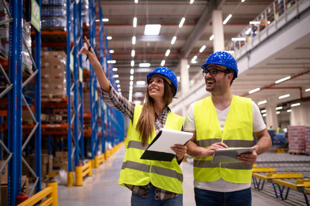 istock Warehouse workers in protective uniform walking through large distribution center organizing goods distribution. Woman employee pointing to the shelves while her coworker using tablet. 1163139797