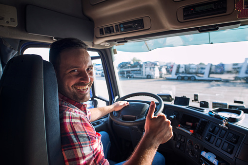 Portrait of truck driver sitting in his truck holding thumbs up. Transportation and trucking services.