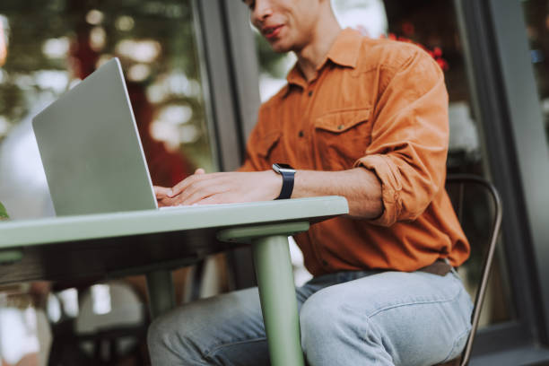 istock Young man in orange shirt using laptop outdoors 1163144265