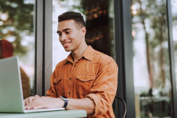 Joyful young man in orange shirt using laptop