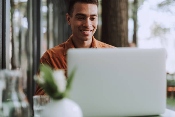 istock Joyful young man sitting at the table and using laptop 1163144274