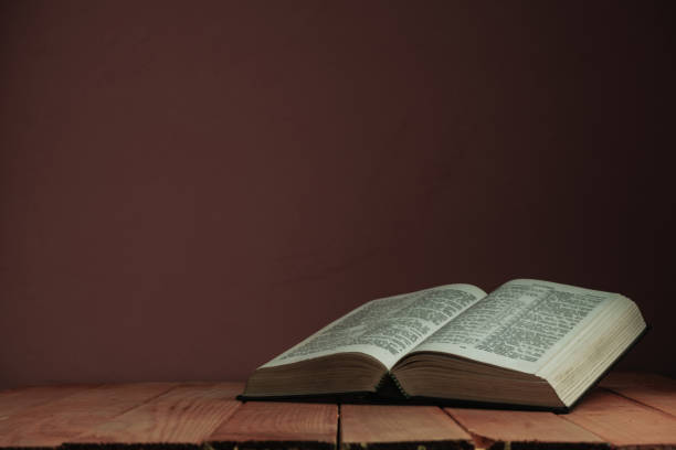 istock Open Holy Bible on a old wooden table. Beautiful red wall backgroround. Religion concept. 1163152260