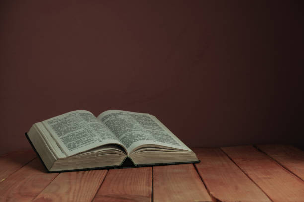 istock Open Holy Bible on a old wooden table. Beautiful red wall backgroround. Religion concept. 1163152476