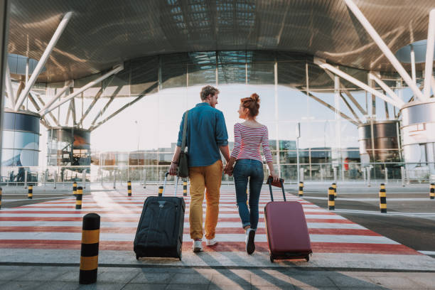 Beautiful loving couple with travel suitcases holding hands in airport Full length back view portrait of young man and his charming girlfriend walking and carrying their trolley bags. They looking at each other and smiling luggage photos stock pictures, royalty-free photos & images