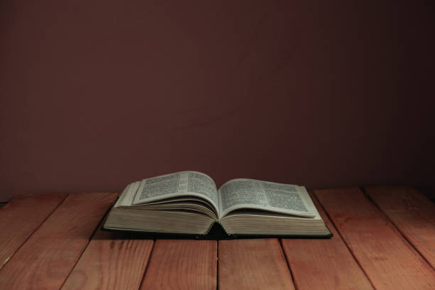 istock Open Holy Bible on a old wooden table. Beautiful red wall backgroround. Religion concept. 1163153416