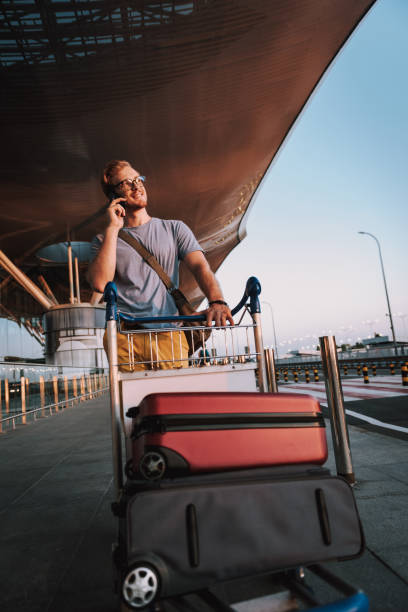 istock Handsome young man with luggage trolley talking on cellphone 1163154888
