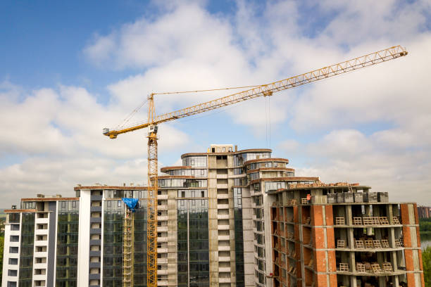 istock Apartment or office tall building under construction. Brick walls, glass windows, scaffolding and concrete support pillars. Tower crane on bright blue sky copy space background. 1163155025