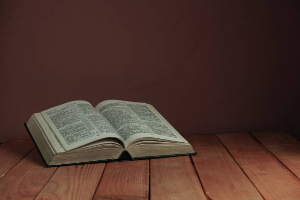 istock Open Holy Bible on a old wooden table. Beautiful red wall backgroround. Religion concept. 1163156445