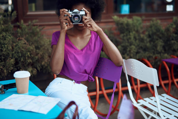 istock Young afro-american lady is using retro camera in cafe 1163156766