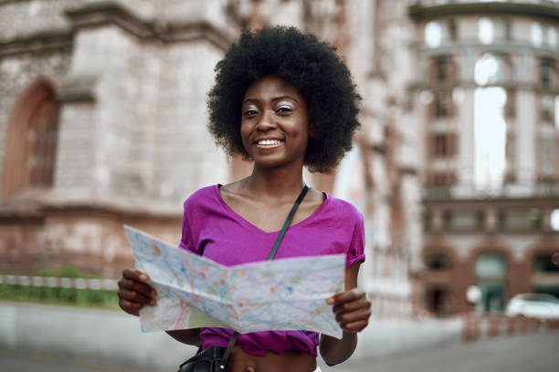 istock Smiling young woman standing on street with map 1163156850